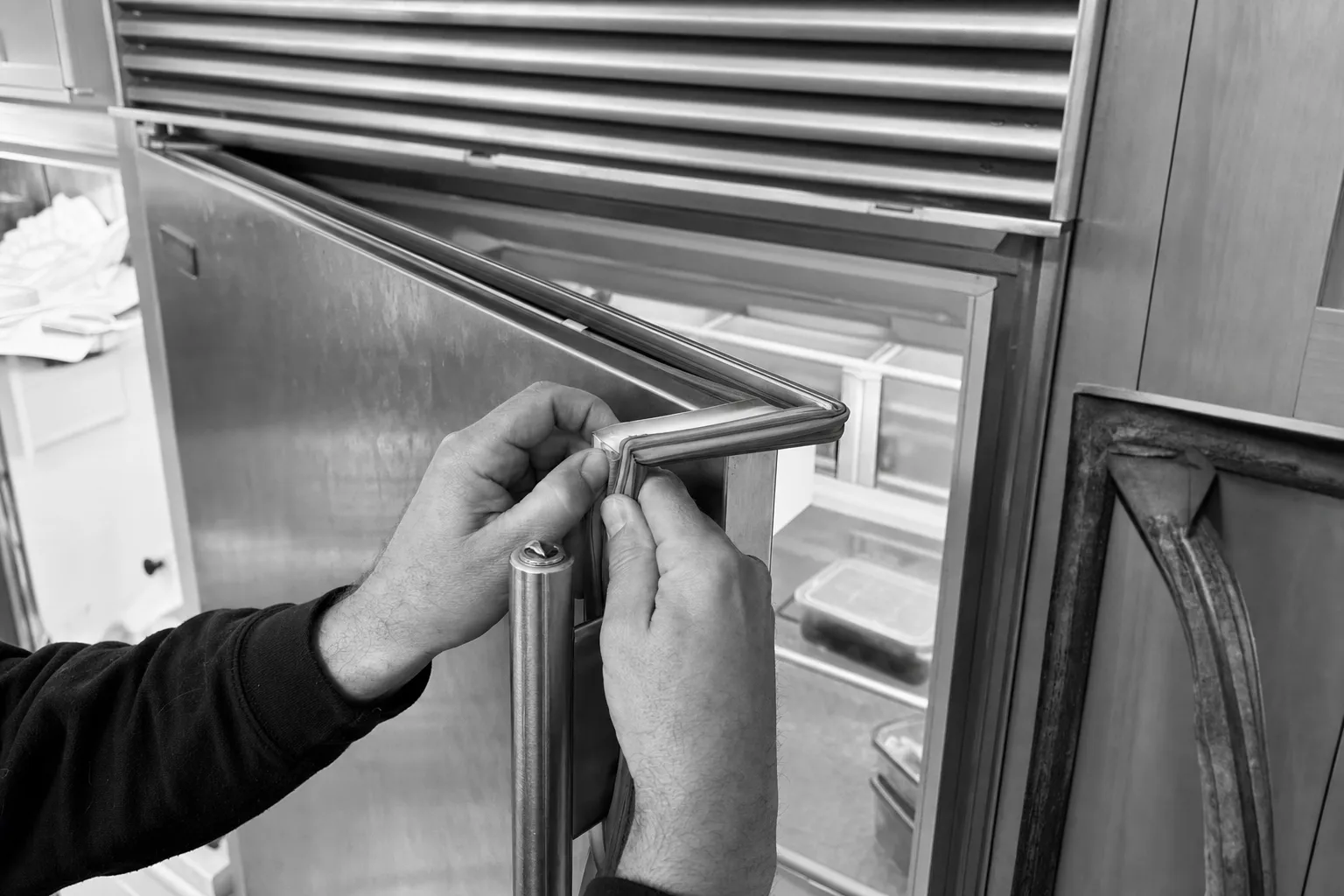 Hands pressing a new magnetic gasket into the door frame of a stainless built-in refrigeration cabinet